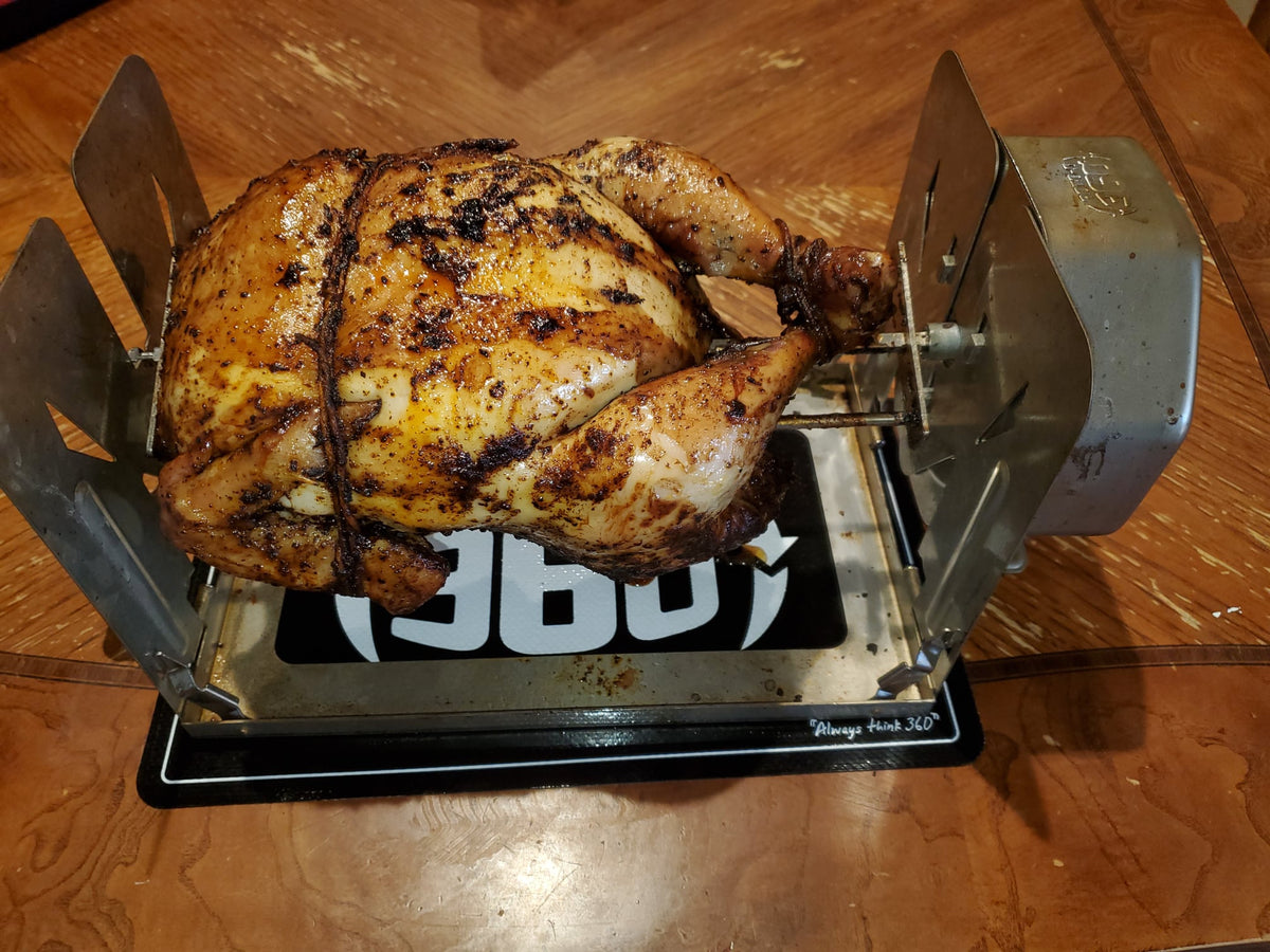 Whole roasted chicken on a ROTO-Q 360 rotisserie setup resting on a ROTO-Q 360 Premium Cooking Mat.
