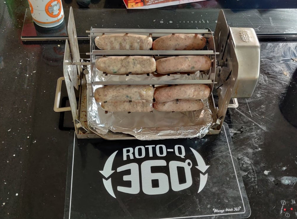 ROTO-Q 360 rotisserie setup holding sausages, resting on a ROTO-Q 360 Premium Cooking Mat.