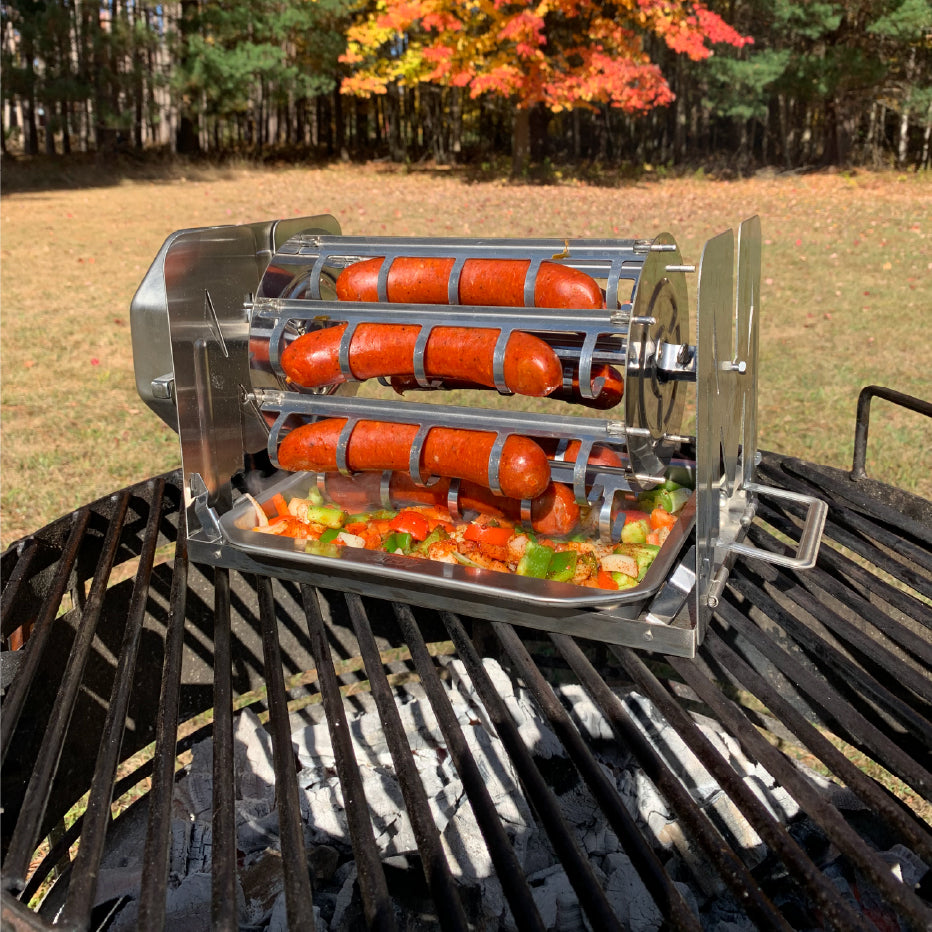 ROTO-Q 360 Sausage Rotisserie holding sausages over an outdoor grill with vegetables in the drip tray.
