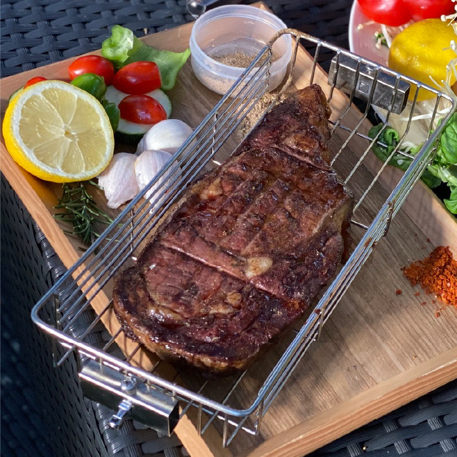 Cooked steak inside a ROTO-Q 360 Rotisserie Cage (Flat) served on a wooden platter with lemon and garnishes.