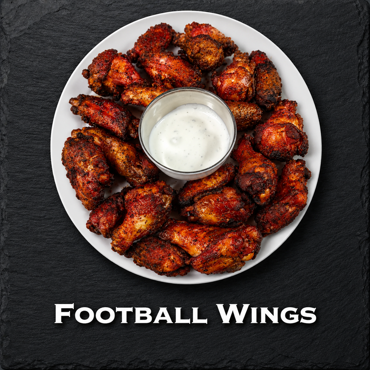 A top-down view of a white plate filled with crispy, reddish-brown football wings arranged in a circle around a small metal cup of white ranch dressing, set on a dark slate background with the text 'FOOTBALL WINGS' below.