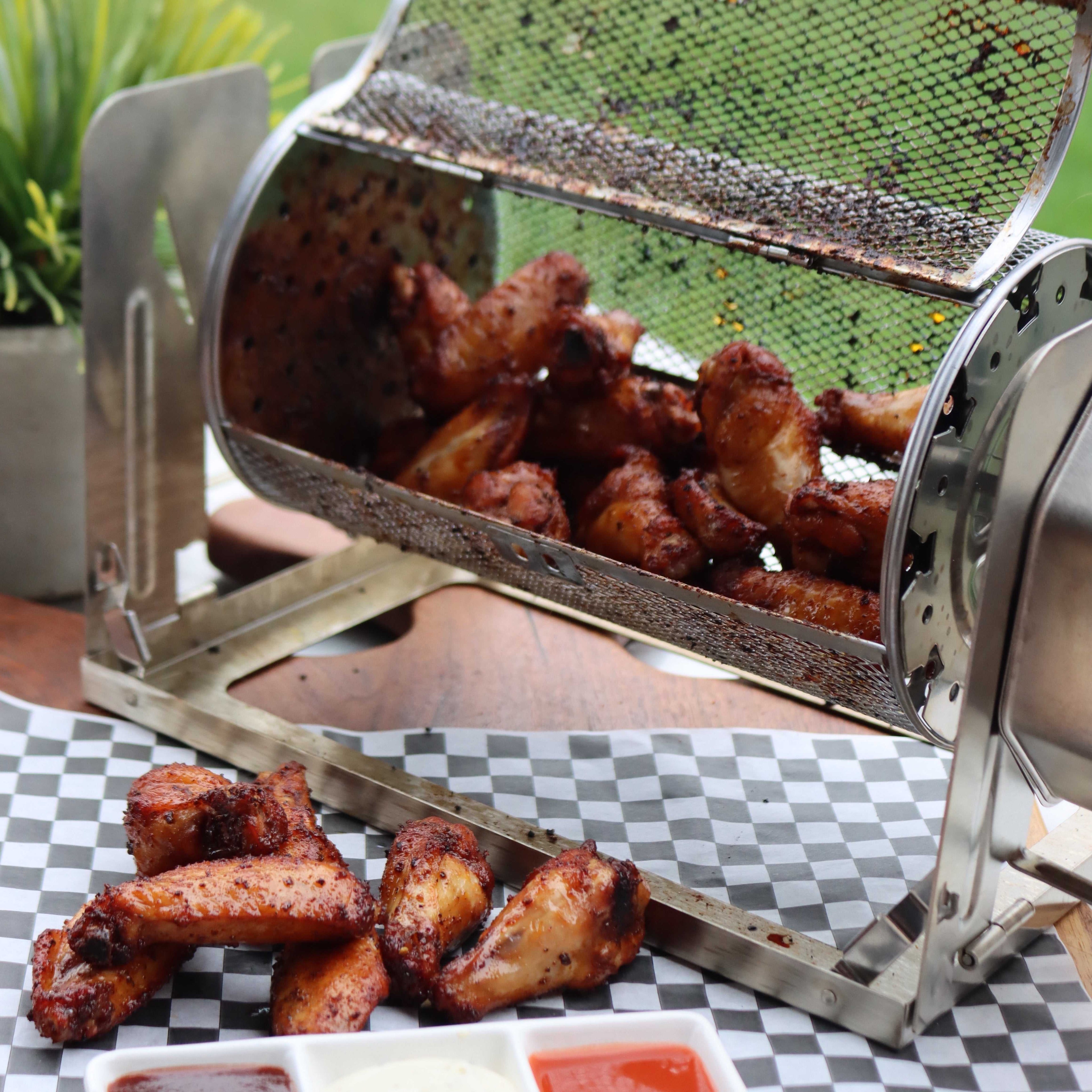 ROTO-Q 360 rotisserie basket (round) filled with cooked chicken wings, served on checkered paper with dipping sauces.