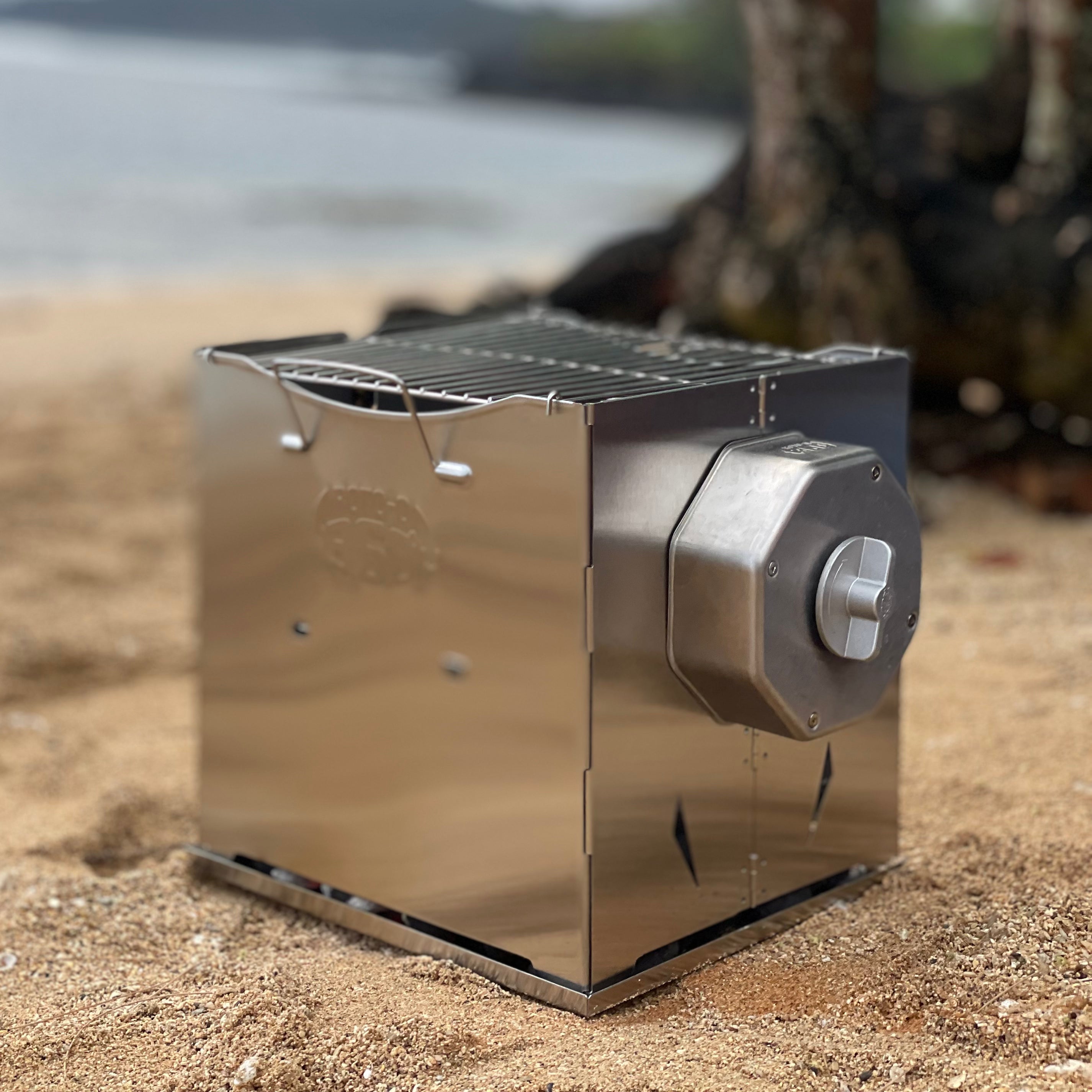 ROTO-Q 360 foldable stainless steel grill set up on a sandy beach.
